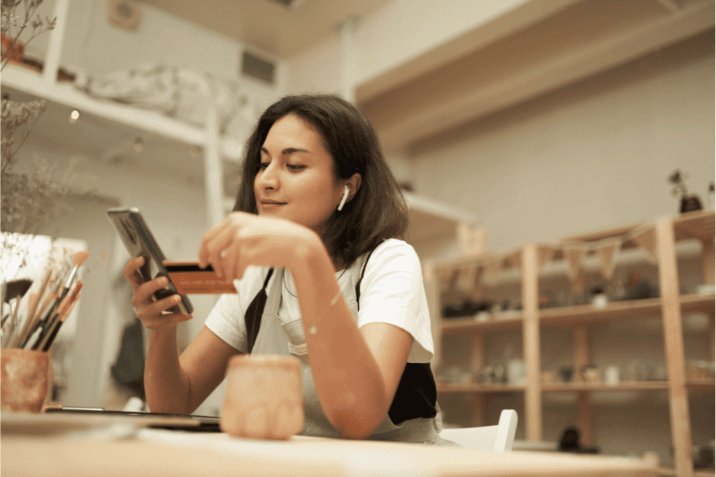 Woman In Pottery Studio Making A Purchase From A Smartphone